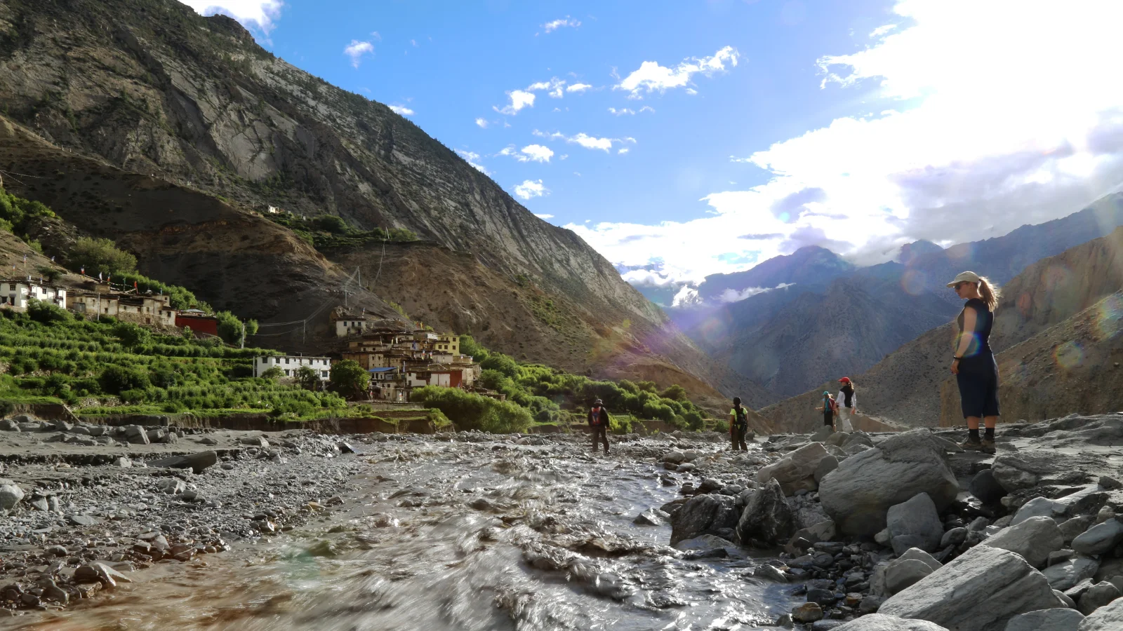 Missionários da JOCUM parados perto de um rio na zona rural do Nepal enquanto uma pessoa atravessa o rio